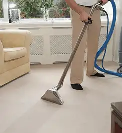 Professional carpet cleaner using a hot-water extraction wand and hose machine in a living room in Albuquerque, NM.