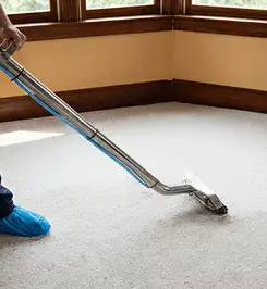 Steam carpet cleaning technician using a hot-water extraction wand on a residential carpet, wearing blue protective shoe covers Albuquerque, NM.