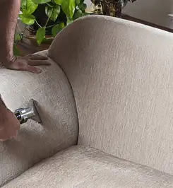 Professional upholstery cleaner deep-cleaning a fabric sofa with a handheld extraction tool and hose Albuquerque, NM.