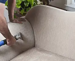 Professional upholstery cleaner deep-cleaning a fabric sofa with a handheld extraction tool and hose in Albuquerque, NM.